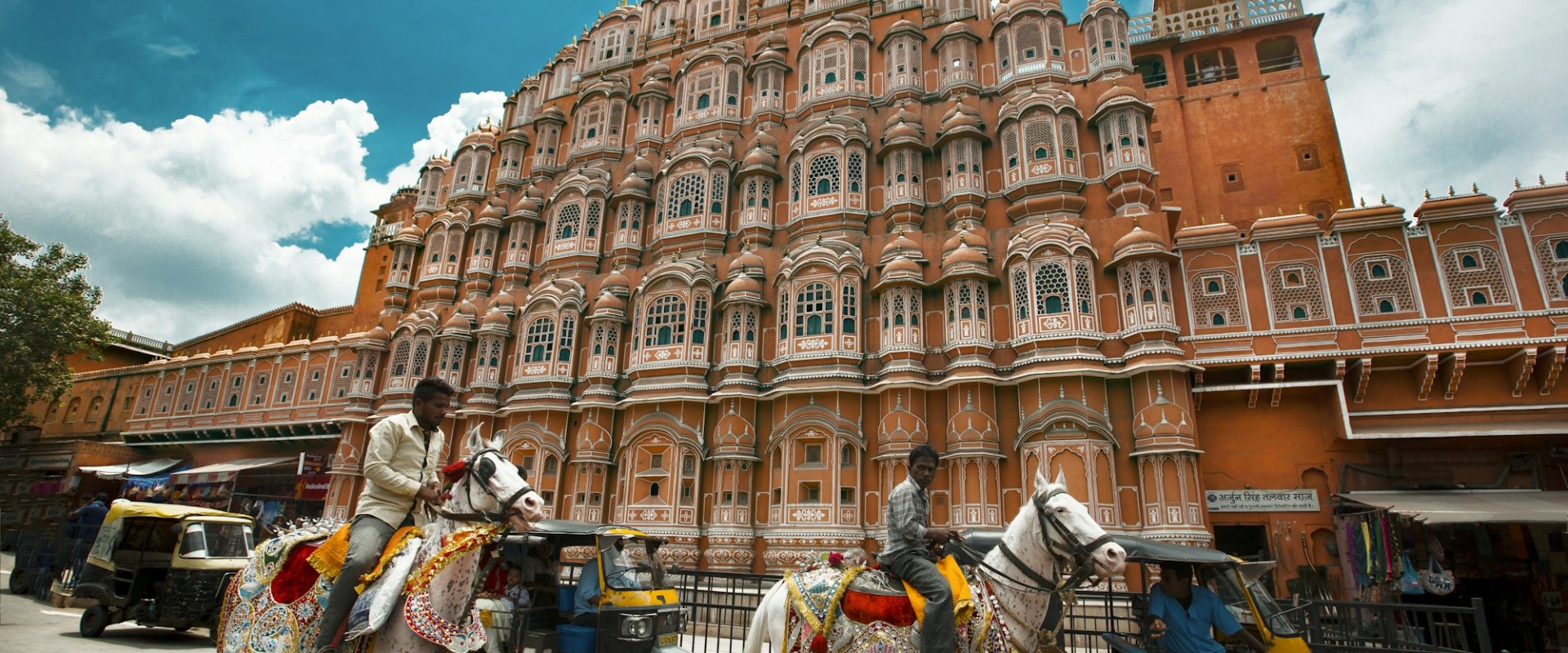 Riders on decorated white horses passing the pink facade of Hawa Mahal in Jaipur