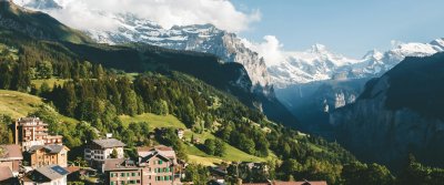Chalets scattered across green Alpine meadows beneath snow-capped Swiss peaks