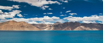 Blue glacial water below brown and snow-streaked Himalayan mountains in Ladakh